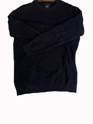 Mörkblå ribbstickad tröja från Lindebergh  - En stilren mörkblå ribbstickad tröja med rund hals och långa ärmar. Tröjan har en enkel och klassisk design som passar till det mesta. Perfekt för dig som gillar en clean och tidlös look.