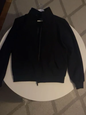 Wool blend ifrån Dressmann - Stilren svart jacka från Dressmann i ullblandning. Jackan har hög krage, dragkedja framtill och ribbade muddar vid ärmslut och nederkant. Perfekt för dig som vill ha en enkel men snygg jacka.