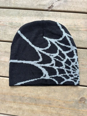 Svart mössa med spindelnätsmönster - Säljer en svart mössa med grått spindelnätsmönster. Mössan är tunn och stretchig, perfekt för dig som vill ha en cool och unik accessoar till hösten eller vintern. Materialet känns mjukt och bekvämt mot huvudet.