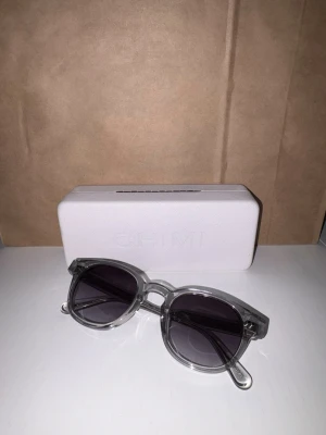 Chimi solglasögon - Säljer ett par äkta Chimi 01. Stilren modell med transparent grå båge och mörka glas som passar till allt.  Bra skick, använda men inga repor på de över huvudtaget . Kommer med original fodral och putsduk. Märken finns på skyddsboxen, men glasögonen är i fint skick.  Nypris runt 1400 kr. Säljes till bra pris. Hör av dig vid frågor eller om du vill ha fler bilder.