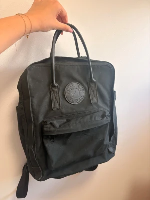 Svart Kånken ryggsäck från Fjällräven - Klassisk svart Kånken ryggsäck från Fjällräven med rund logotyp framtill. Ryggsäcken har ett stort huvudfack, framficka med dragkedja, två sidofickor och bärhandtag upptill. Tillverkad i slitstark syntetväv med justerbara axelband. Rymmer 16 liter!