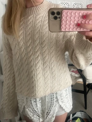 Beige kabelstickad tröja - Säljer en beige kabelstickad tröja med rund hals och långa ärmar. Tröjan har ett klassiskt flätmönster och är gjord i ett mjukt, tjockt material. Snygg till höst och vinter 