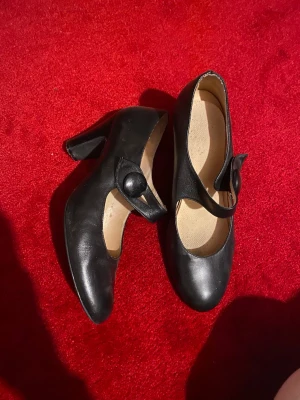 Svarta Mary Jane-pumps med klack - söta svarta vintage Mary Jane klackar i skinn med rund tå. har en rem över foten som kan öppnas. passar ca st 38-39