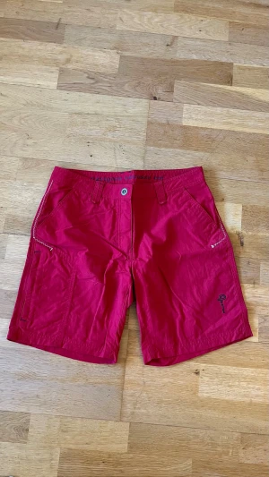 Röda shorts från Pelle P - Snygga röda shorts från Pelle P med normal passform och praktiska fickor fram och bak. Tillverkade i slitstark bomull, perfekta för sommardagar. Klassisk design med bälteshällor och knappstängning framtill. Ingår bälte.