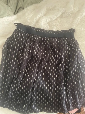 Svart kortkjol från ONLY med mönster - Kortkjol från ONLY i svart med vita prickiga detaljer. Kjolen har resår i midjan och ett lätt, luftigt tyg som ger en snygg volym. Perfekt för dig som gillar en enkel men ändå trendig look.