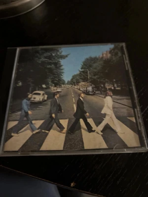 The Beatles Abbey Road CD - CD-skiva med albumet Abbey Road av The Beatles. Omslaget visar det ikoniska övergångsstället med bandmedlemmarna. Skivan är silverfärgad med svart text och levereras i ett plastfodral.