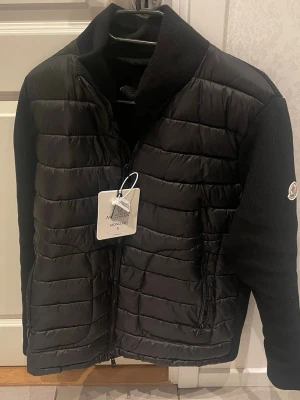 Helt ny svart  Moncler cardigan strl S/M -  Säljer en svart cardigan i väldigt fint skick – helt ny och aldrig använd. Märkt som storlek S, men passar även M beroende på passform. Den sitter bra i längden som en S, men är lite rymligare runt armar och midja.  Perfekt för dig som vill ha en clean och stilren look som funkar till allt.    Pris: 1899 kr