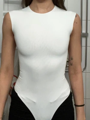 Vit ärmlös body med rund hals - Snygg vit body med rund halsringning och ärmlös design. Tillverkad i ett stretchigt och mjukt material som sitter tight mot kroppen och framhäver figuren. Perfekt att styla med jeans eller kjol för en clean och modern look.