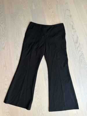 Svarta utsvängda kostymbyxor - Snygga svarta kostymbyxor med utsvängda ben och hög midja. Byxorna har en klassisk look och är perfekta för dig som gillar stilrena plagg med lite edge. Materialet ser ut att vara en mjuk och följsam mix, troligen polyester eller viskos.