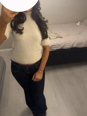 Vit stickad kortärmad polotröja - Säljer en vit stickad polotröja med korta ärmar och ribbade kanter. Tröjan har en croppad passform och är gjord i ett mjukt material som känns skönt mot huden. Perfekt att styla med jeans eller kjol för en clean look. Använd en gång.