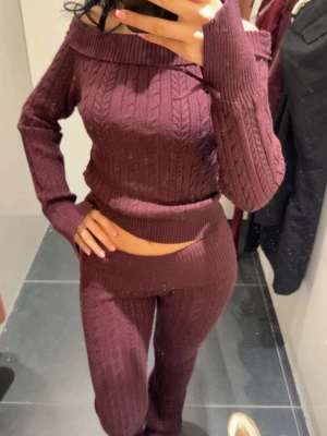 Vinrött stickat loungewear-set - Mysigt vinrött loungewear-set med off shoulder-tröja och matchande byxor. Setet är ribbstickat med kabelstickat mönster och har långa ärmar samt hög midja på byxorna. Perfekt för chill dagar hemma. Materialet känns mjukt och stretchigt.(Använt en gång)