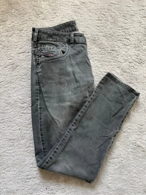 Diesel jeans - Snygga grå slim fit jeans från Diesel med klassisk femficksdesign och diskreta slitningar. Jeansen har en smal passform och är tillverkade i ett mjukt denimtyg med stretch för extra komfort. Perfekta för dig som gillar en modern och avslappnad stil.