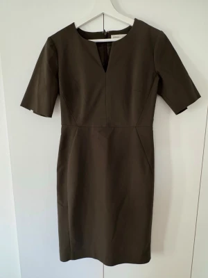 Mörkgrön klänning  - Stilren khakigrön fodralklänning med korta ärmar. Klänningen är figurnära och knälång samt har en slits och dold dragkedja bak. Endast använd ett fåtal gånger. 