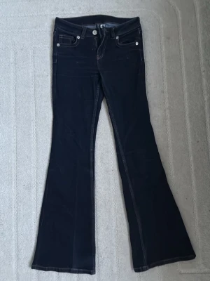 Mörkblå bootcut jeans  - Snygga mörkblå bootcut jeans med vita kontrastsömmar och klassiska fem fickor. Jeansen har låg midja och utsvängda ben, perfekta för en trendig och avslappnad look. Materialet känns mjukt och stretchigt för extra komfort.