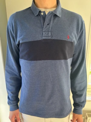 Polo Ralph Lauren Pikétröja  - Snygg Polo Ralph Lauren tröja. Blåmelerade färg med en marinblå rand och snygga unika armbågslappar ger tröjan en riktigt go look och karaktär. 🧵 Märke: Polo Ralph Lauren 📏 Storlek: M. Klassisk passform. 🧩 Material: 100% Bomull 📐 Mått: Axel: 48 cm. Bröst: 56 cm. Ärm: 67 cm. Längd: 73 cm. ✅ Skick: 9/10. Fint skick, sparsamt använd. Inga defekter!  🧍‍♂️ Modellen är 189 cm (dubbelkolla måtten ovan för att avgöra) 💰 Nypris: Ca 1400 kr ‼️ Skickas inom 24h‼️