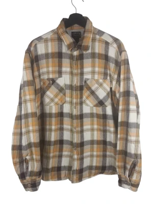 Stüssy Heavyweight Plaid Work Shirt, storlek L - Rutig skjorta med långa ärmar och knäppning framtill. Skjortan har två bröstfickor med knappar och en liten logotypetikett på vänster ficka. Ärmsluten är försedda med knappar. Insidan av skjortan är fodrad med ett vitt våffelmönstrat tyg. Armhåla till armhåla: 58cm Axelbredd: 48cm Långt: 71cm Armlängden från armhåla: 49cm