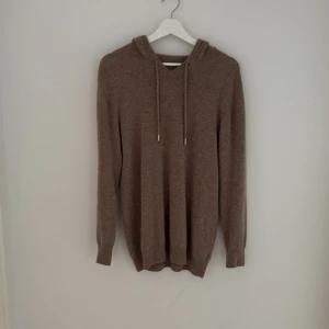 Beige stickad hoodie med huva - Mysig beige stickad hoodie med huva och snörning framtill. Tröjan har långa ärmar och ribbade muddar vid ärmslut och nederkant. Perfekt för lager-på-lager och chill dagar. Tröjan är i oanvänt skick. Pris kan diskuteras!