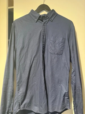 Mörkblå skjorta Dressmann Slim Fit - Mörkblå långärmad skjorta från Dressmann i slim fit-modell. Skjortan har button-down krage och en bröstficka på vänster sida. Tillverkad i mjukt tyg som ger en avslappnad men ändå stilren look.