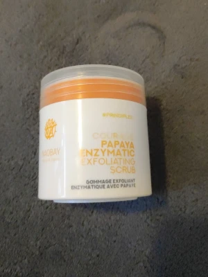 Naobay Papaya Enzymatic Scrub - En enzymatisk exfolierande skrubb från Naobay med papayaextrakt. Förpackningen är vit med orange detaljer och har en rund form. Perfekt för att fräscha upp huden och ge lyster.