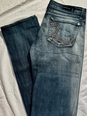 Rock & Republic Castello Jeans | W27 L34 | Y2K Vintage Premium Denim - Säljer ett par exklusiva Rock & Republic i modellen Castello. Jeansen är i absolut nyskick/oanvända utan några som helst tecken på slitage eller slitna benslut. En perfekt mörkblå tvätt med hög kvalitet och lyxig känsla. Mycket eftertraktad modell för den rätta Y2K-looken! Mått / Measurements: * Waist (Midja): 40 cm (flat) * Inseam (Innerben): 85 cm (Great for tall people! / L34) * Length (Längd): 110 cm * Leg opening (Benvidd): 19 cm * Material: 98% Cotton, 2% Elastane (Comfortable stretch)