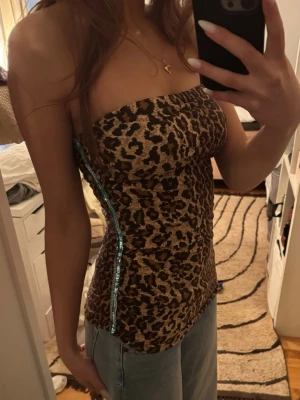 Leopardmönstrad tubtopp med paljetter - Säljer en leopardmönstrad tubtopp med en snygg detalj av blå paljetter längs sidan. Toppen är åtsittande och axelbandslös, perfekt för dig som vill sticka ut. Materialet känns mjukt och stretchigt, vilket gör den bekväm att bära.