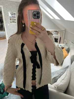 Krämvit stickad kofta med svart band - Från Y.A.S i storlek L men passar mig som är S/M!💕 Söt krämvit stickad kofta med strukturmönster och vågiga kanter. Koftan har trekvartsärmar och knyts framtill. 