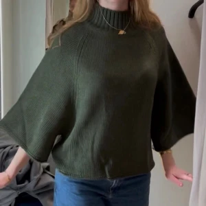 Mörkgrön stickad ponchotröja - Snygg mörkgrön stickad ponchotröja med hög hals och vida trekvartsärmar. Väldigt bra skick då den är använd ca 2 gånger. Jätte bekväm och snygg. Passar även större storlekar. 
