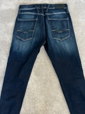 Mörkblå Replay jeans med kontrastsömmar - Snygga mörkblå jeans från Replay med slitningar och kontrastsömmar. Modellen har raka ben, fem fickor och coola detaljer på bakfickorna. Perfekta för dig som gillar en avslappnad men trendig stil.
