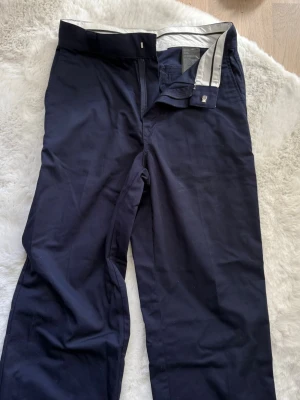 Mörkblå chinos från H&M Divided - Snygga mörkblå chinos från H&M Divided med klassisk rak passform. Tillverkade i en mjuk bomullsblandning med polyester för extra komfort. Perfekta för dig som vill ha en stilren och enkel look. Stängs med dragkedja och knapp.