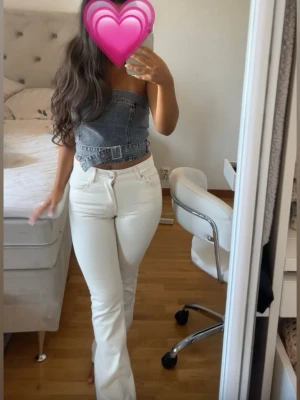 Grå denim tubtopp med bälte - Trendig grå tubtopp i denim med cool bältdetalj i midjan. Toppen är axelbandslös och har en croppad passform som ger en edgy look. Perfekt att styla med höga jeans eller kjol för en modern vibe.