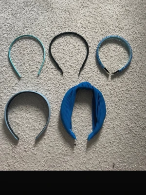 Mix av blå och svarta diadem - Säljer ett set med fem diadem i olika blå nyanser och svart. Diademen har olika former och material, från smala plastmodeller till ett bredare tygdiadem med twistad knut. Perfekt för att variera din look och matcha med olika outfits.