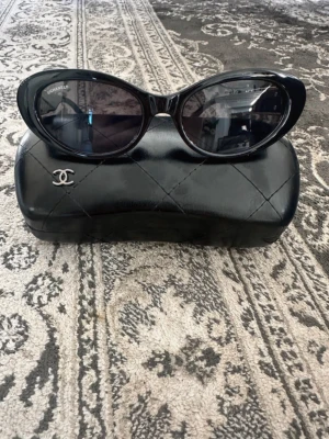 Svarta solglasögon med gulddetaljer - Säljer ett par ikoniska svarta solglasögon  med rundad form och breda skalmar. Solglasögonen har guldfärgade kedjedetaljer. Kommer med matchande svart fodral med quiltad look.
