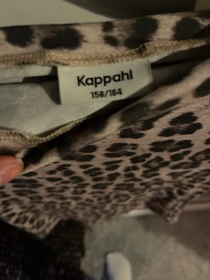 Leopardmönstrad t-shirt från Kappahl - Säljer en snygg leopardmönstrad t-shirt från Kappahl i beige och svart. T-shirten har korta ärmar och är tillverkad i mjukt material som känns skönt mot huden. Perfekt för dig som vill sticka ut med ett djurmönster i garderoben.