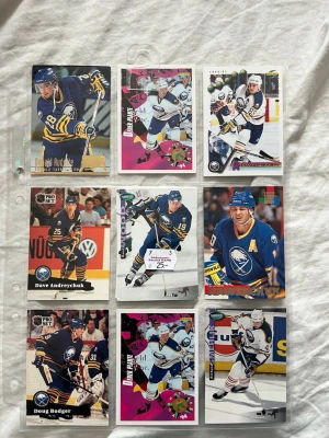 Samling Buffalo Sabres hockeykort - Säljer en samling med nio Buffalo Sabres hockeykort i plastficka. Korten visar olika spelare i matchställ, både i blå och vit uniform. Blandade märken som Pro Set och Upper Deck. Perfekt för dig som gillar NHL och samlar på sportkort.