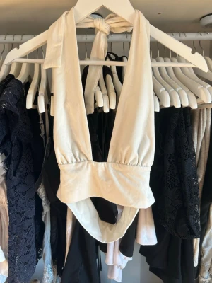 Beige omlott halterneck topp - Trendig beige halterneck topp med omlott och knyt i nacken. Toppen är ärmlös och har en djup urringning framtill. Perfekt för att styla med höga jeans eller kjol. Materialet känns mjukt och stretchigt, troligen bomull eller syntet.