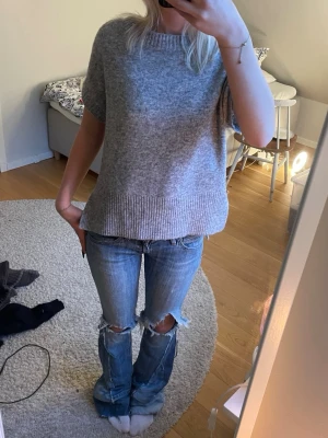 Grå stickad tröja från Sand Copenhagen  - Mjuk och stilren grå stickad tröja från Sand Copenhagen med korta ärmar och bred ribbad kant vid ärmslut, nederkant och halsringning. Perfekt till jeans eller kjol för en avslappnad look.