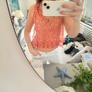 Blommig volangtop i rött och rosa - Söt blommig linnetopp i rött och rosa med volangkant nertill och v-ringad hals. Toppen är ärmlös och har en luftig, croppad passform som passar perfekt till sommaren. Perfekt för dig som gillar romantiska detaljer och lätta material. Passar S!