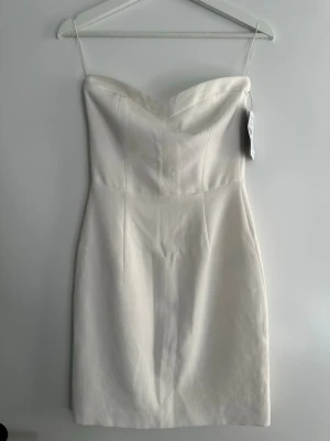 Vit axelbandslös klänning Zara - Säljer en stilren vit axelbandslös klänning från Zara. Klänningen har figurnära passform och en snygg sweetheart-urringning. Passar bra som studentklänning!