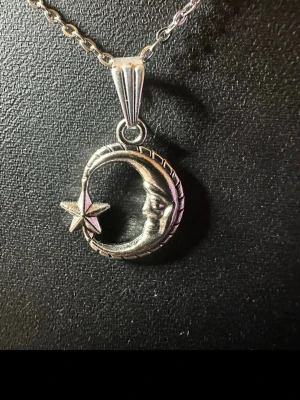 Silverhalsband med måne och stjärna - Unikt halsband i silverfärgad metall med ett hänge format som en måne med ansikte och en liten stjärna bredvid. Kedjan är tunn och klassisk, och hänget har fina detaljer som ger ett mystiskt och coolt intryck. Perfekt för dig som gillar rymdtema och snygga accessoarer.