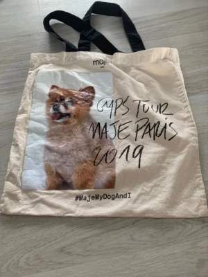 Beige tygkasse från Maje Paris - Trendig beige tygkasse från Maje med svart text 'Gyps Tour Maje Paris' och ett stort tryck av en söt hund på framsidan. 