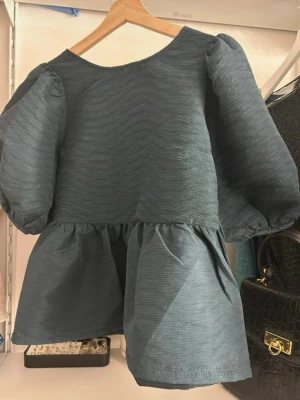 Mörk grön blus med puffärmar och knyt - Supersöt mörkgrön blus från Carin Wester med puffiga ärmar och volang nedtill. Blusen har en v-rigning i ryggen med knytband och är helt oanvänd! Orginal priset är 599kr men säljer för 250kr!