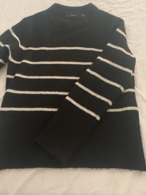 Svart stickad tröja med vita ränder - Snygg svart stickad tröja från vero Moda med vita horisontella ränder. Tröjan har rund halsringning och långa ärmar. Perfekt för dig som gillar en klassisk och enkel stil med en twist. Materialet känns mjukt och bekvämt.