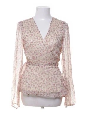 Blommig omlottblus med långa ärmar - Söt omlottblus i transparent, ljusbeige tyg med små rosa blommor. Blusen har långa ärmar, v-ringning och knytband i midjan för en feminin siluett. Perfekt för dig som gillar romantisk och bohemisk stil.