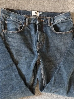 Blå jeans från 157 New Classic - Säljer ett par klassiska blå jeans från 157 New Classic. Jeansen har fem fickor, raka ben och tydliga kontrastsömmar. Tillverkade i slitstark denim med en snygg tvättad look. Perfekta för dig som gillar en enkel och tidlös stil. 30w 32L