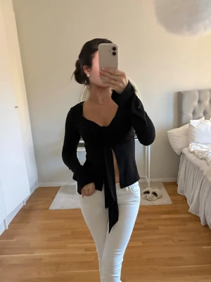 Svart topp  - Trendig svart omlottopp med lång ärm och snygg knytning framtill. Toppen har en djup v-ringning och är figurnära med lätt croppad passform. Använd 1 gång!!!!  