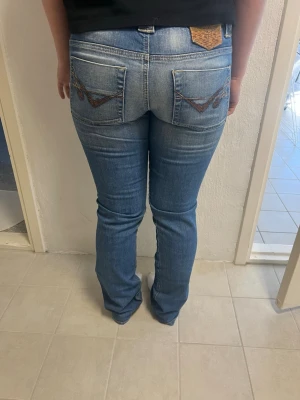 Ljusblå tajta bootcut jeans med brodyr - Säljer ett par ljusblå bootcut jeans med snygg brodyr på bakfickorna och klassisk femficksmodell. Jeansen har normal/low midja. Dom är vero moda från långt tillbaka 