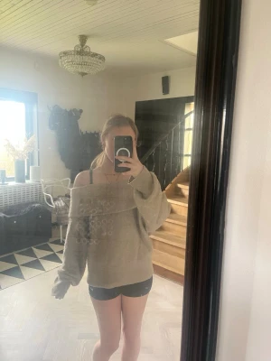 Beige off shoulder stickad - Beige stickad tröja med bred off shoulder-krage och långa ärmar. Tröjan har en avslappnad och oversized passform, vilket ger en chill vibe. Materialet ser mjukt och fluffigt ut, perfekt för lager på lager under höst och vinter.
