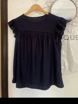 Mörkblå blus med volangärm - Söt mörkblå blus med broderade detaljer och volangärmar. Perfekt för en trendig look. Köpt i en marknad i Spanien. Ingen prislapp 