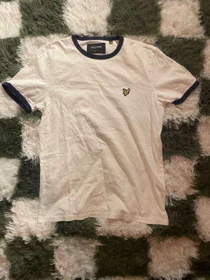Vit t-shirt från Lyle & Scott - Vit t-shirt från Lyle & Scott med mörkblå ribbade kanter vid hals och ärmslut.  Perfekt till jeans eller shorts för en clean och enkel stil.   Pris diskuteras gärna! 