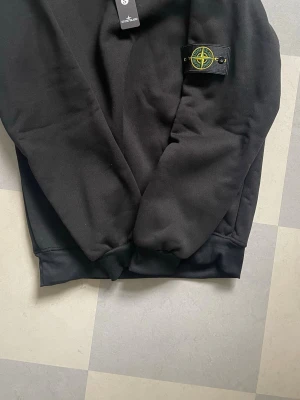 Svart sweatshirt från Stone Island - Säljer en svart sweatshirt från Stone Island med den klassiska badgen på ärmen. Tröjan har rund halsringning, ribbade muddar och är tillverkad i mjukt bomullsmaterial. Priset är diskutabelt och hör gärna av dig ifall du har fler frågor!